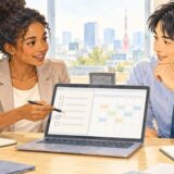 Two coworkers review a handover checklist and calendar together at an office table